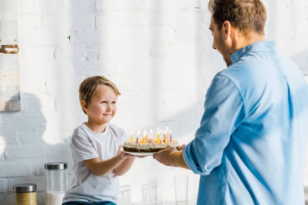 Father giving birthday cake to adorable preschooler son in kitchen — Stock Photo