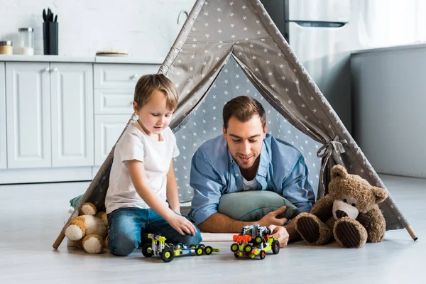 Father and preschooler son playing with toy cars and teddy bears under wigwam at home — Stock Photo