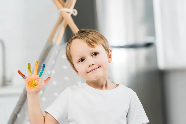 Adorable smiling preschooler boy with colorful paint on hand looking at camera at home — Stock Photo