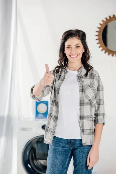 Mujer en camisa gris mostrando el pulgar hacia arriba en la lavandería - foto de stock