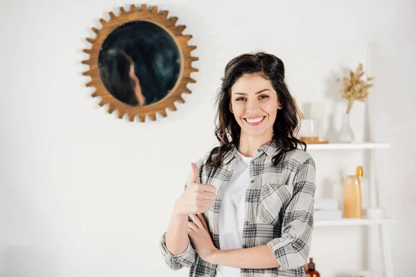 Mujer en camisa gris mostrando el pulgar hacia arriba y sonriendo en casa - foto de stock