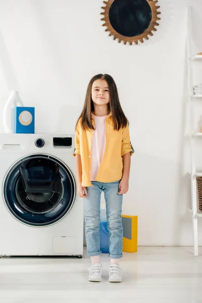 Enfant en chemise jaune et jeans debout dans la buanderie — Photo de stock