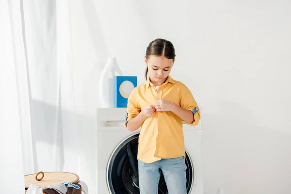 Criança de pé e descompactando camisa amarela na lavanderia — Fotografia de Stock
