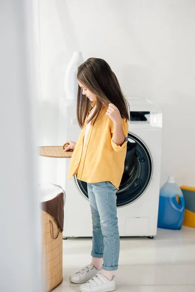 Child standing and holding basket cover in laundry room — Stock Photo