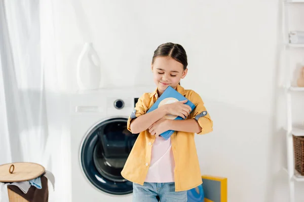 Child in yellow shirt holding washing powder in laundry room — Stock Photo