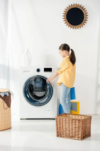 Side view of child in yellow shirt near basket opening washer in laundry room — Stock Photo