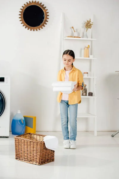 Kind in gelbem Hemd und Jeans hält Handtücher vor Leiter in Waschküche — Stockfoto