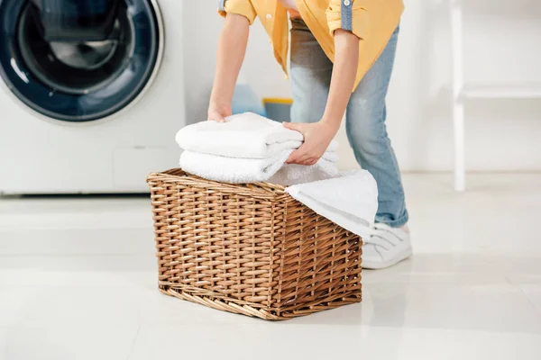 Abgeschnittene Ansicht des Kindes in der Nähe der Waschmaschine, die Handtücher in den Korb in der Waschküche legt — Stockfoto