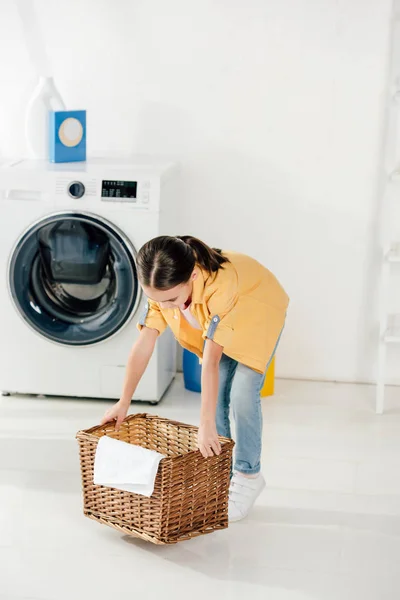Дитина в жовтій сорочці біля пральної машинки бере кошик у пральні — стокове фото