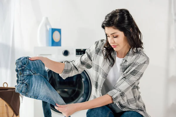 Femme près de laveuse tenant un jean enfant dans la buanderie — Photo de stock