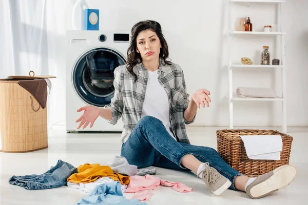Mulher cansada sentada no chão perto de roupas espalhadas e cestas na lavanderia — Fotografia de Stock