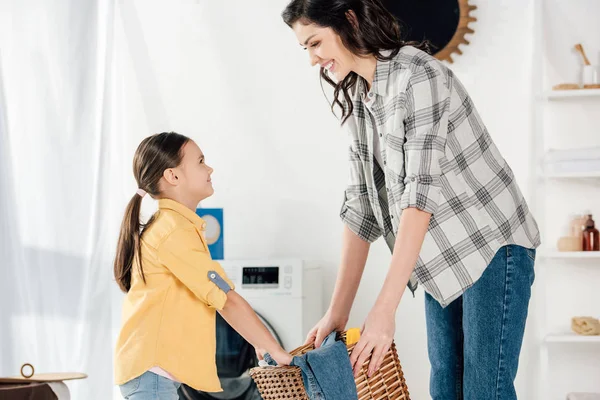 Daughter in yellow shirt and mother in grey shirt holding basket in laundry room — Stock Photo