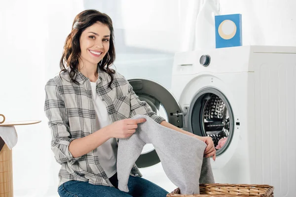 Frau hält Kleidung in Waschküche neben Waschmaschine — Stockfoto