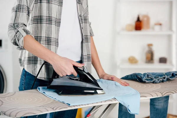 Vista recortada de mujer en camisa gris planchado en lavadero - foto de stock