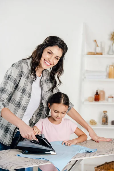 Mère en chemise grise et fille en t-shirt rose repassage à la maison — Photo de stock