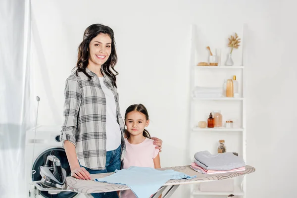 Mother and daughter standing near ironing board in laundry room — Stock Photo