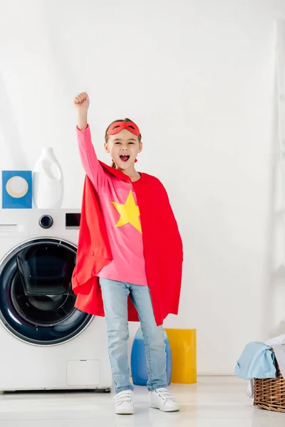 Child standing in red homemade suit with star sign and showing celebrating in laundry room — Stock Photo