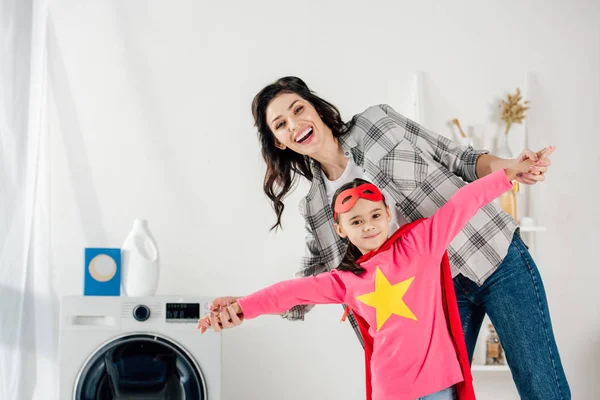 Mutter im grauen Hemd und Tochter im roten selbstgebastelten Anzug mit Sternzeichen amüsieren sich in der Waschküche — Stockfoto