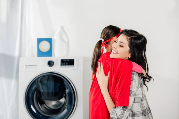Mutter umarmt Tochter im roten hausgemachten Anzug mit Sternzeichen in der Waschküche — Stockfoto