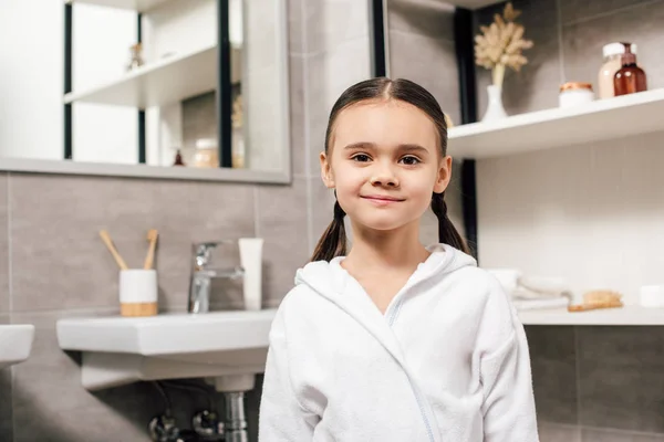 Selective focus of cute child in white bathrobe in bathroom — Stock Photo
