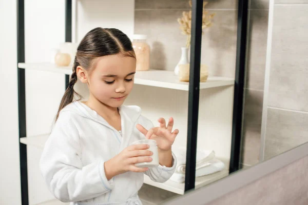 Selective focus of child in white bathrobe with cosmetic cream in bathroom — Stock Photo