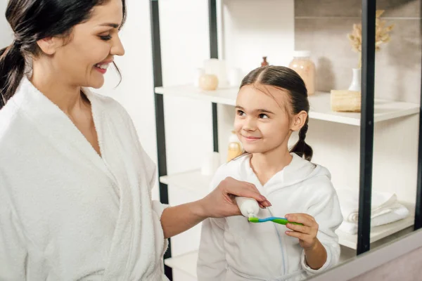 Mère appliquant du dentifrice sur la brosse à dents fille dans la salle de bain — Photo de stock
