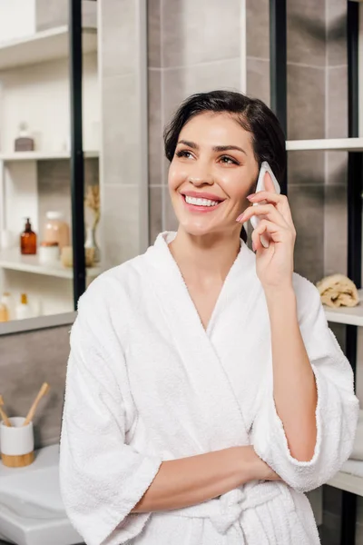 Woman in bathrobe talking on smartphone in bathroom — Stock Photo