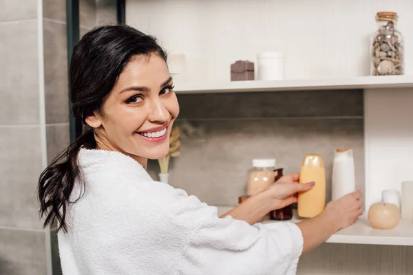 Mulher tomando garrafas com gel de chuveiro de prateleiras no banheiro — Fotografia de Stock