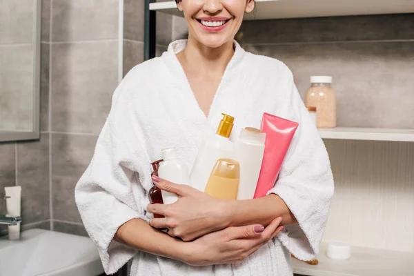 Cropped view of woman in white bathrobe holding bottles in bathroom — Stock Photo