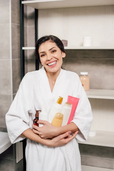 Woman in white bathrobe holding bottles in bathroom — Stock Photo