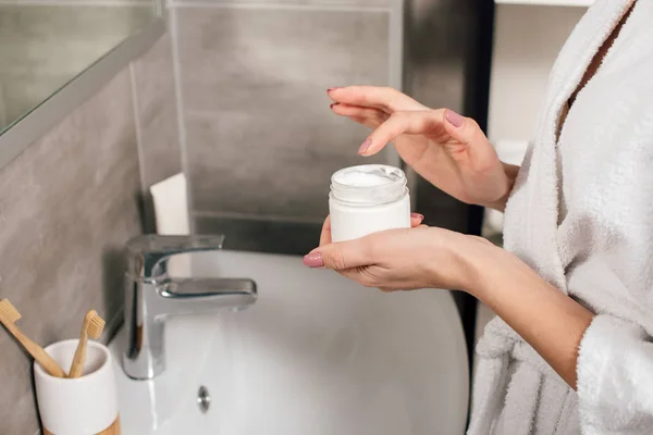 Vue recadrée de femme tenant récipient avec crème cosmétique dans la salle de bain — Photo de stock