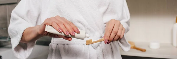 Панорамный снимок женщины, наносящей зубную пасту на зубную щетку в ванной комнате — стоковое фото