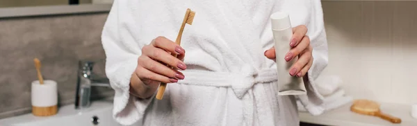 Panoramic shot of woman holding toothpaste and toothbrush in bathroom — Stock Photo