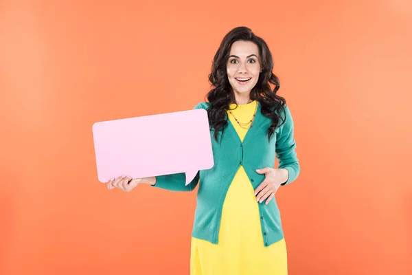 Surprised smiling pregnant woman holding speech bubble isolated on orange — Stock Photo