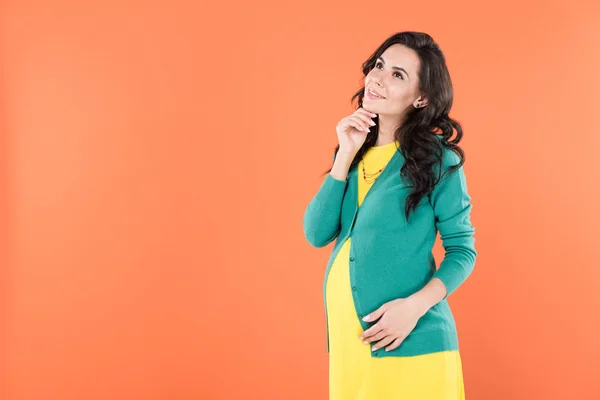 Donna incinta pensierosa con i capelli ricci guardando con sorriso isolato su arancione — Foto stock