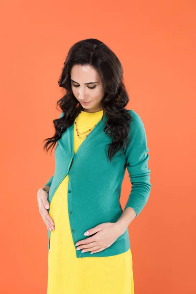 Bella bruna donna incinta in vestiti casual toccare pancia isolato su arancione — Foto stock