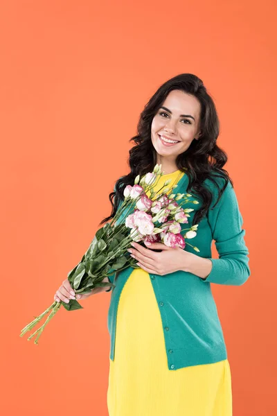 Hermosa mujer embarazada rizada sosteniendo ramo de flores aislado en naranja - foto de stock