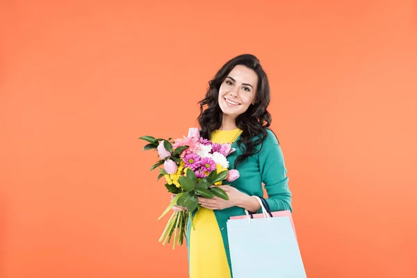 Curly pregnant woman holding flower bouquet and shopping bags isolated on orange — Stock Photo