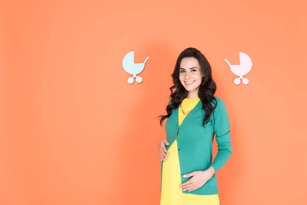 Excited brunette pregnant woman in green cardigan touching belly on orange background — Stock Photo