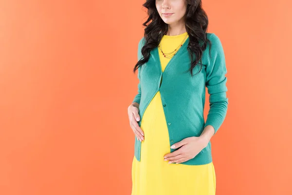 Частичный взгляд на кудрявую беременную женщину, касающуюся живота, изолированного от апельсина — стоковое фото