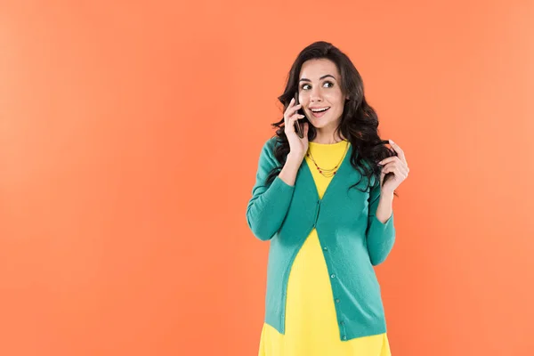 Mujer embarazada alegre hablando en smartphone y jugando con el pelo rizado aislado en naranja - foto de stock