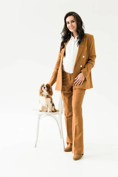 Vista completa de la mujer embarazada en traje marrón con perro sobre fondo blanco - foto de stock