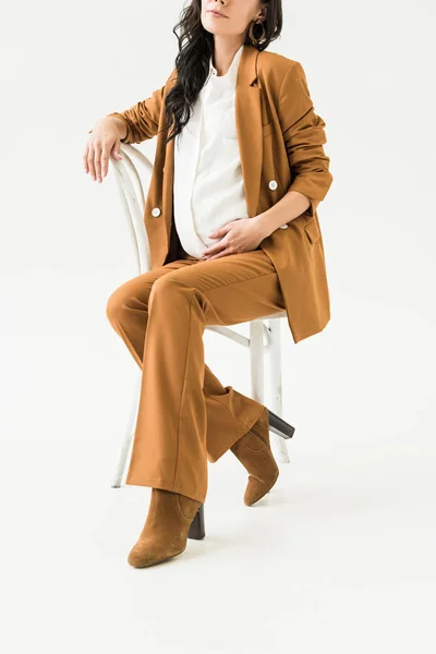 Partial view of stylish pregnant woman in suit sitting on chair on white background — Stock Photo