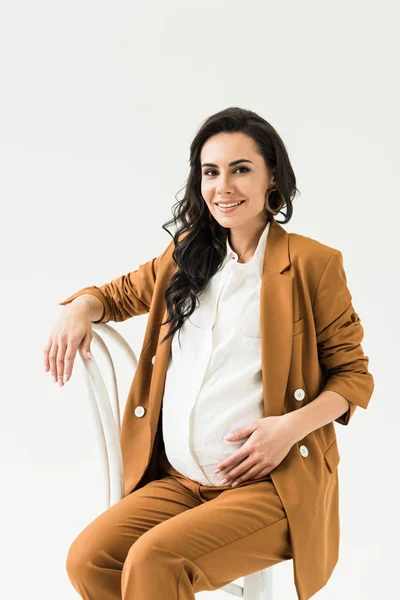 Brune souriante femme enceinte assise sur une chaise isolée sur blanc — Photo de stock