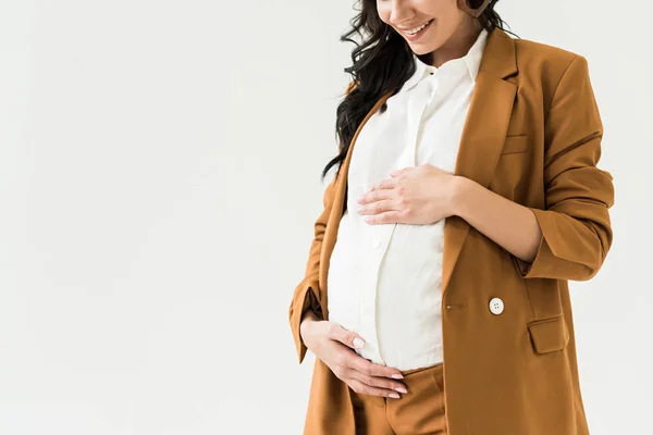 Abgeschnittene Ansicht einer lachenden Schwangeren im braunen Anzug, die Bauch isoliert auf Weiß berührt — Stockfoto