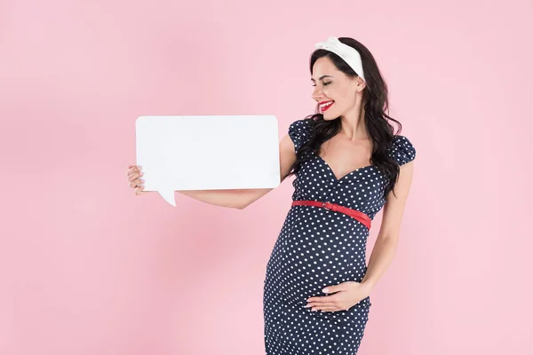 Pretty pregnant woman holding speech bubble and touching belly on pink background — Stock Photo