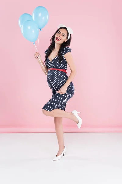 Wunderschöne schwangere Frau mit Luftballons, die auf einem Bein auf rosa Hintergrund stehen — Stockfoto