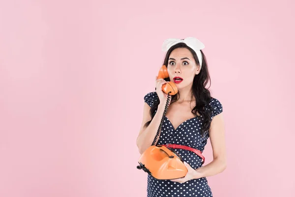 Удивлённая беременная женщина в разукрашенном платье разговаривает по телефону изолированному на розовый — стоковое фото