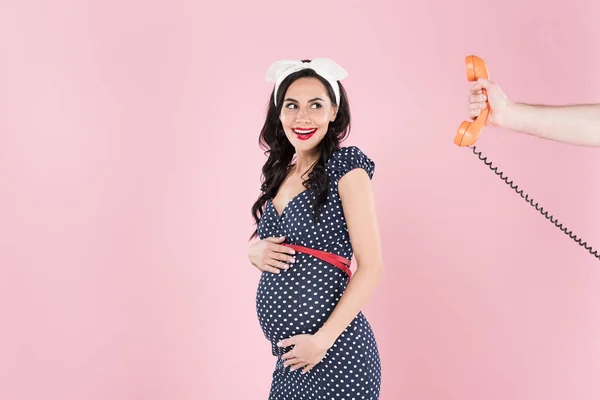 Rire femme enceinte regardant récepteur téléphonique isolé sur rose — Photo de stock