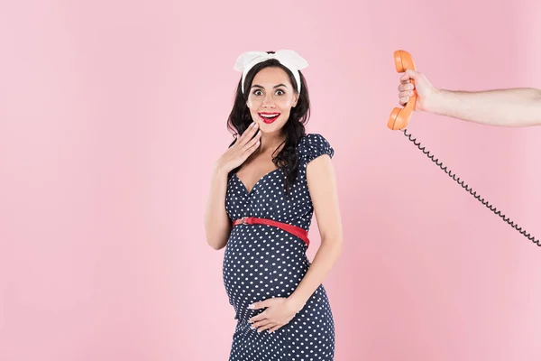 Fröhliche schwangere Frau im Kleid, das Bauch berührt, isoliert auf rosa — Stockfoto